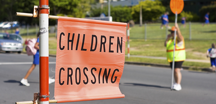 Sign saying childrens crossing erected outside a school where children are crossing a road