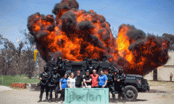 Declan, family and members from the AFP stand in front of the bearcat with an explosion in the background.